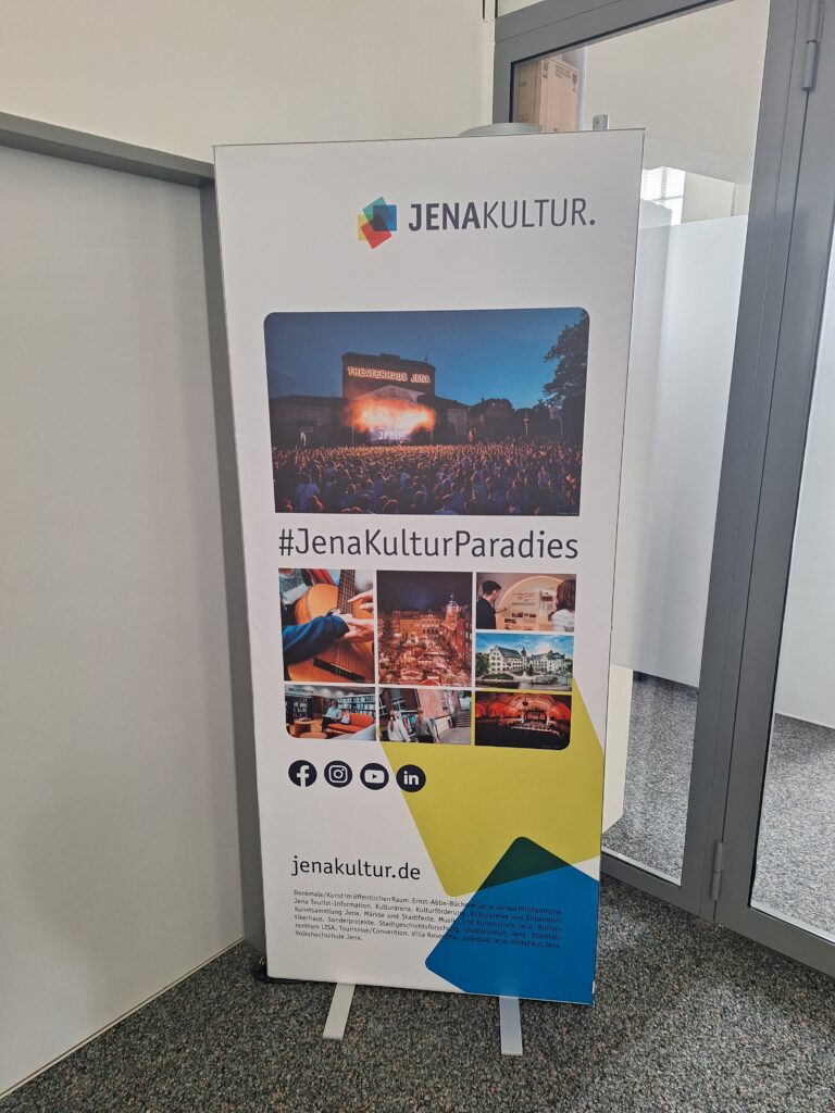 Ein beleuchtbares Rollup mit einer Bildercollage von den JenaKulturEinrichtungen, dem #JenaKulturParadies, dem JenaKultur-Logo, der jenakultur.de, Social-Media-Icons.