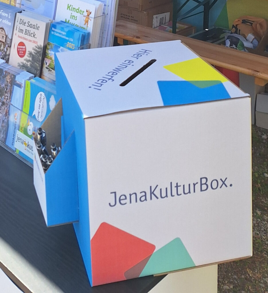 Eine Box mit blauen, gelben, roten und grünen Würfeln mit Schlitz zum Einwerfen von Teilnahmeblättern und einem Flyerhalter,