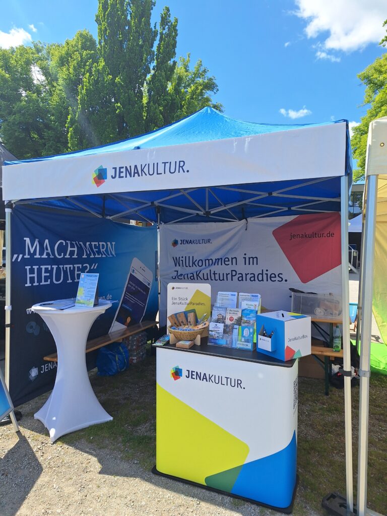 Ein Pavillon mit JenaKultur-Wechselbanner an der Front, Hintergründen zur Bewerbung des Jena Veranstaltungskalenders und einer Rückwand mit JenaKultur-Branding.
